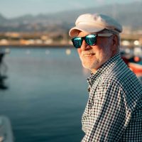 handsome-senior-man-casual-shirt-hat-sitting-port-looking-boats-sea-relaxed-elderly-bearded-male-wearing-sunglasses-enjoying-travel-retirement